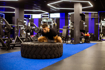 Man doing tire flips in a modern gym with vibrant lighting and equipment