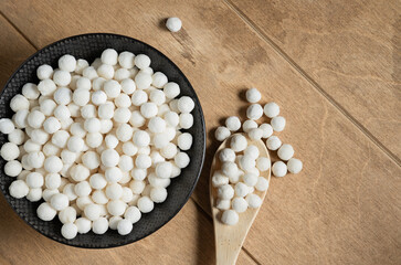 Organic tapioca pearls in black bowl on wooden table top view. Spoon with white dry tapioca pearls, cooking ingredient, gluten-free food, healthy eating.