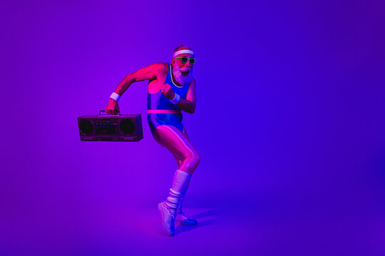 Energetic senior man in retro jumpsuit dancing with a boombox under purple blue neon lights for fitness lifestyle and retro inspired stock image