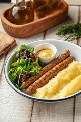 Grilled sausages served with mashed potatoes, mustard and fresh green salad on a white plate