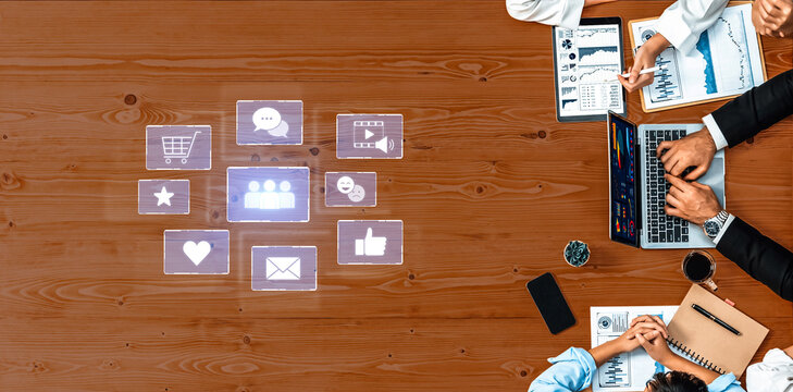 A top-down view of a business meeting with professionals discussing digital marketing strategies, showcasing laptops, data analytics, and social media icons on a wooden table. Trope