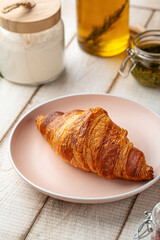 Golden crispy croissant served on pink plate on wooden table with warm morning light