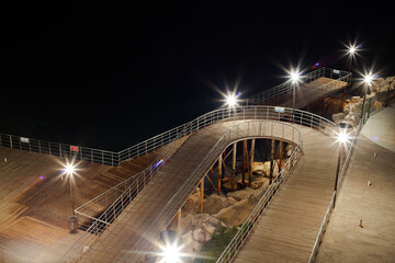Wooden pier and walkways built on metal poles by the sea. The wooden pier and walkway are illuminated at night.