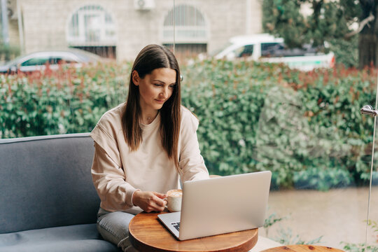 Woman working on a laptop at a cafe, sipping coffee by a window for a calm, productive scene