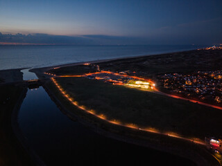 Aerial twilight view of coastal town streetlights trace canal and curved shoreline, glowing path leads to illuminated buildings, serene water and distant horizon blend natural calm with urban order.