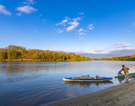 Man is standing on the beach next to a blue kayak - Powered by Adobe
