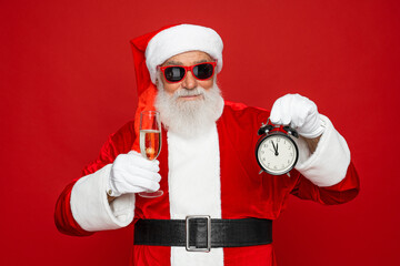 Photo of retired old man grey beard funky holding clock full glass golden wine drink having fun open mouth wear santa x-mas costume suspender sunglass cap isolated red color background