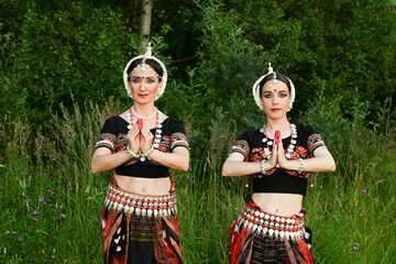 Indian female dancers in beautiful costumes on a green background of nature in a park in dance poses