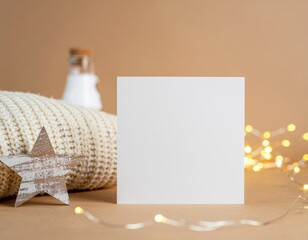 Square blank paper card near white knitted sweater, wooden Christmas decor and lights, copy space. Winter atmospheric mock up, family greeting in rustic or scandinavian style