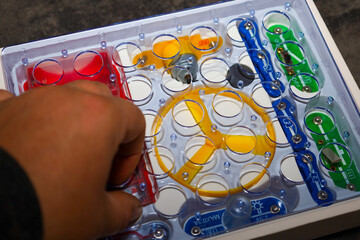 ​This close-up shot features an educational electronics kit with multi-colored components arranged in a plastic tray. A cropped hand is placing or adjusting a red component, highlighting the concept o