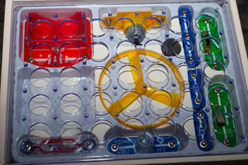 ​This shot displays an educational electronics kit in a clear plastic tray, filled with bright components such as red blocks and a yellow propeller. 