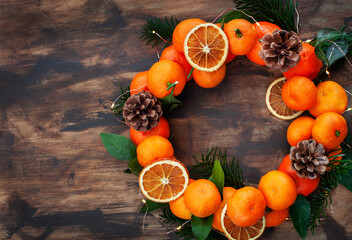 Wreath of fresh ripe tangerines with leaves and cones, on wooden background, top view