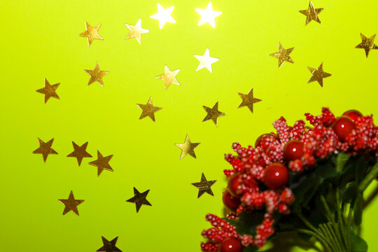 This bright, celebratory close-up shot features golden stars twinkling against a neon-lime green background, alongside a blurred cluster of red berries and foliage.