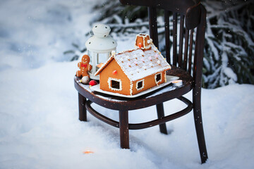 Gingerbread house and holiday decoration on chair in snow winter outdoor background