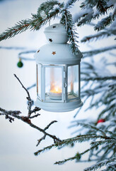 Christmas lantern with candle on branch of snowy winter tree, outdoors