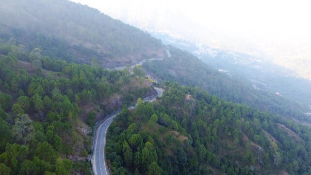 Drone footage capturing the scenic Chandigarh-Shimla Highway and solan valley in the Himalayan foothills, features cars and trucks moving along the winding asphalt road, flanked by dense green forests
