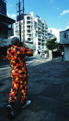 Man in floral outfit photographs a white building under a blue sky.