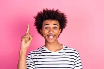 Young man pointing upwards with a joyful expression against a pink background, promoting positivity and creative ideas