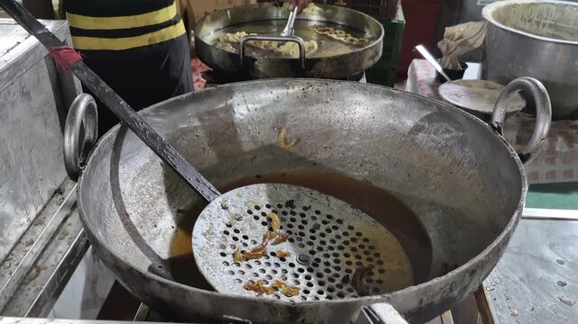 A man fries Indian sweets jalebi in a pan with hot oil, forming circular golden patterns during cooking.