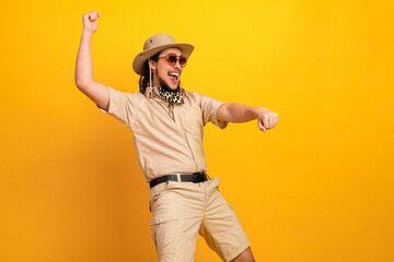Happy explorer wearing safari outfit dances with energy against bright yellow backdrop showcasing...