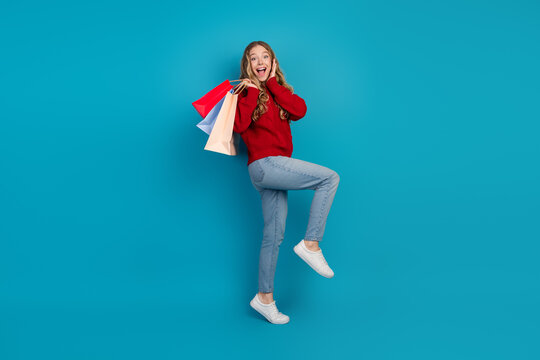 Adorable and cheerful young woman holding shopping bags while posing against blue background