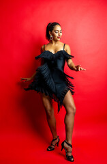 Woman dancing salsa in black fringe dress on red background