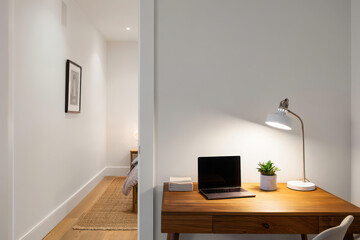 Modern home office desk with laptop, lamp, and plant, bright residential interior