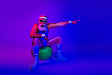 Energetic elderly man in retro fitness outfit poses on a green ball under purple blue neon lights