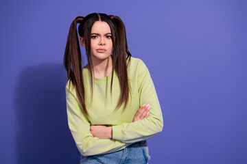 Young woman in casual outfit posing against purple background with arms crossed reflecting expressive attitude