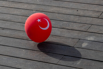 A vibrant red Turkish flag balloon with star and crescent symbol resting in sunlight on wooden deck during Republic Day celebration, creating festive atmosphere. Antalya, Turkey.


