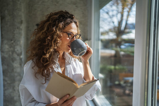 Woman enjoying morning coffee and reading book at home - Powered by Adobe