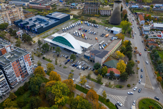 Aerial view of the Kor&ccedil;&euml; bus terminal surrounded by autumn trees, city streets and nearby buildings under soft seasonal light.