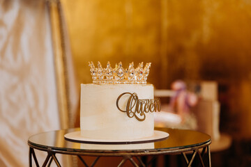 White birthday cake with golden crown and Birthday Queen topper on elegant party table