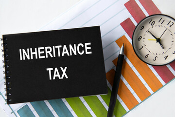 INHERITANCE TAX - words on a black notebook with a chart and alarm clock in the background