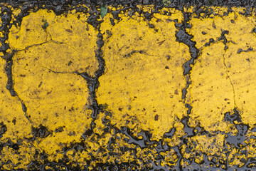 A close-up of old yellow road markings on wet asphalt. The thick layer of paint is cracked and worn. Background. Texture.