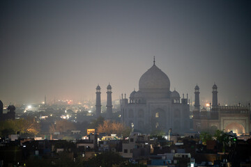 Naklejka premium Late evening dusk night shot of the silhouette dark Taj Mahal with the orange lights of the city showcasing it in Agra India