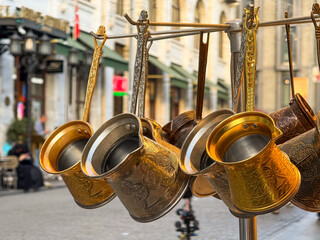 Close-up view of traditional brass Turkish coffee pots with engravings hanging outside a Sirkeci souvenir shop