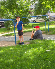 Boys aged 7 and 10 play on a slide at a playground in summer.