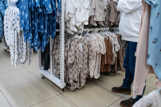Baby clothing section in a store with an expectant parent browsing through racks of cute outfits. Various colors and patterns displayed, showcasing a variety of choices for newborns.