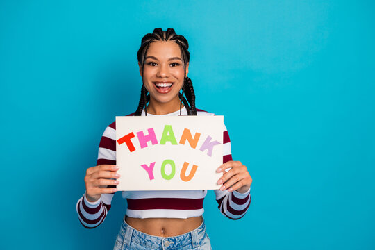Young woman with colorful thank you sign smiles at the camera against a bright blue background expressing gratitude and appreciation
