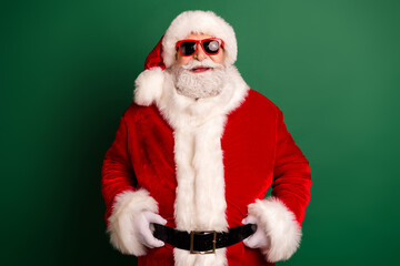 Santa in red suit with white fur hat and sunglass poses in front of green background ready for Christmas season