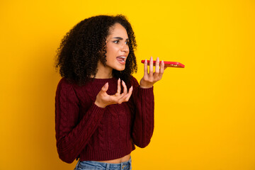 Young mixed race woman shouts into a red megaphone against a bright yellow background expressing urgency and excitement