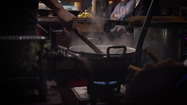 Slow motion showing an illuminated row of yatai food stalls with diners eating under warm lights at night in Fukuoka, Japan, creating a cozy street food atmosphere