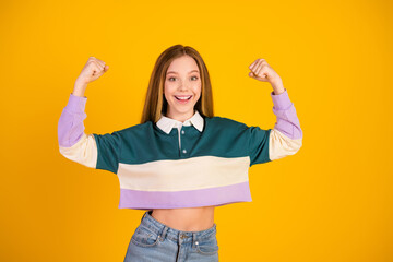 Young woman in casual colorful sweatshirt against yellow background showing strong arm gestures...