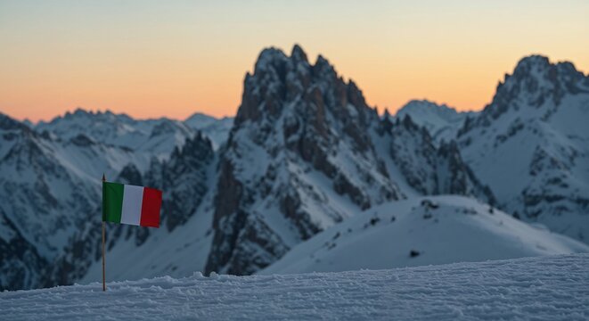 An Italian flag stands proudly in pristine white snow, framed by a majestic backdrop of rugged, snow-capped mountains under a vibrant sunset sky.