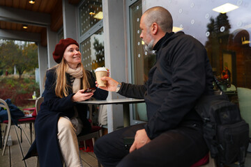 Man and woman sipping coffee on a terrace during fall season, peaceful moment of outdoor relaxation and travel.