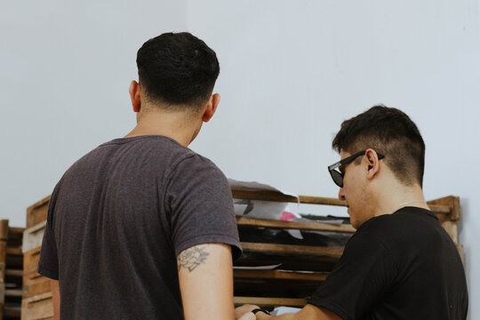 Two young men, artists, learning and collaborating in an art studio, reviewing designs during a creative workshop
