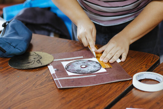 Person cutting paper using a utility knife and ruler, creating art for a college project or workshop