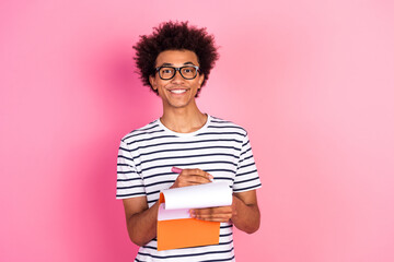 Young man in striped shirt smiling with notebook against pink background, showing confidence and positivity