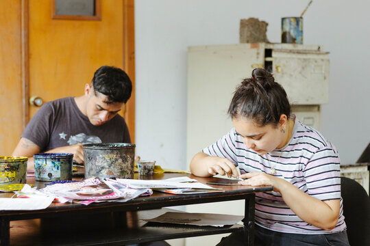 Art students creating printmaking designs during a workshop, focusing on their crafting techniques in a studio